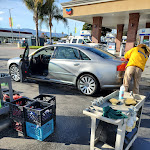 A silver sedan with its door open beside a cart of supplies, with a gas station canopy behind it